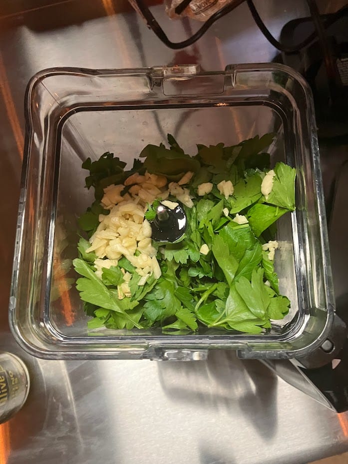 Parsley leaves and minced garlic cloves arranged in the blender, ready to be blended into a flavorful chimichurri sauce.