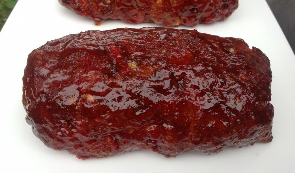 Delicious glazed meatloaf with a glistening exterior, drizzled with a savory sauce, ready on the cutting board to be sliced up